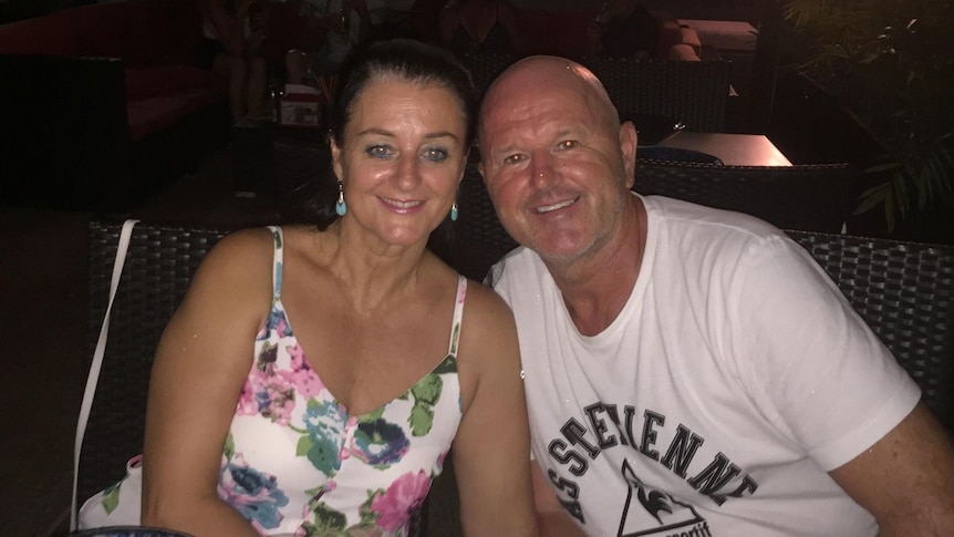 A couple sit at a dinner table and smile at the camera.