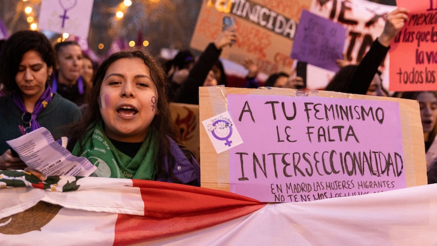A demonstrator holds a sign that reads "Your feminism lacks intersectionality"