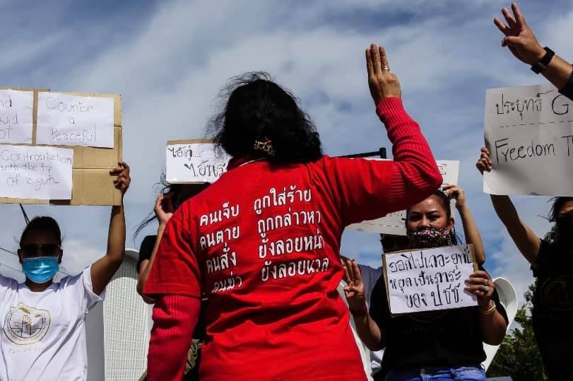 A woman holds up a three-finger salute and wears a red shirt with Thai script.