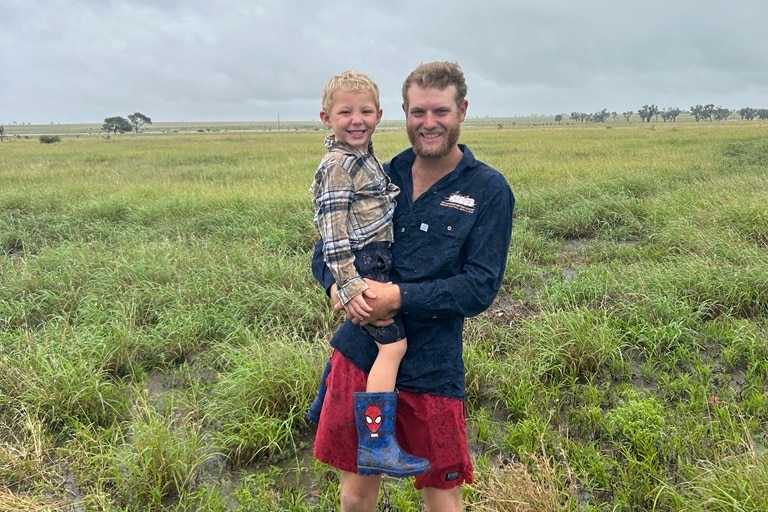 a man holding his young son in a sodden paddock