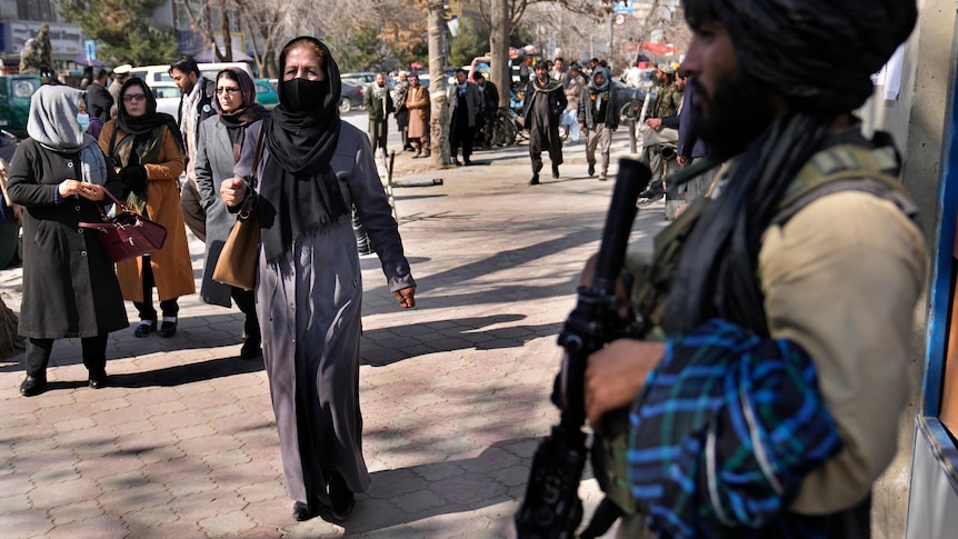 A woman walking past a man with a gun. 