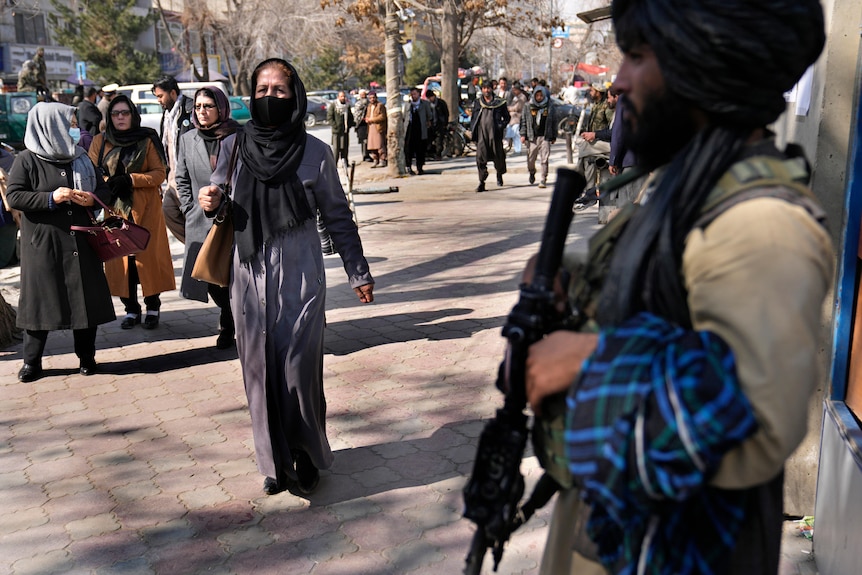 A woman walking past a man with a gun. 