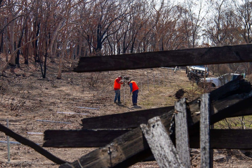 Two men dressed like surveyors stand in a blackened field.