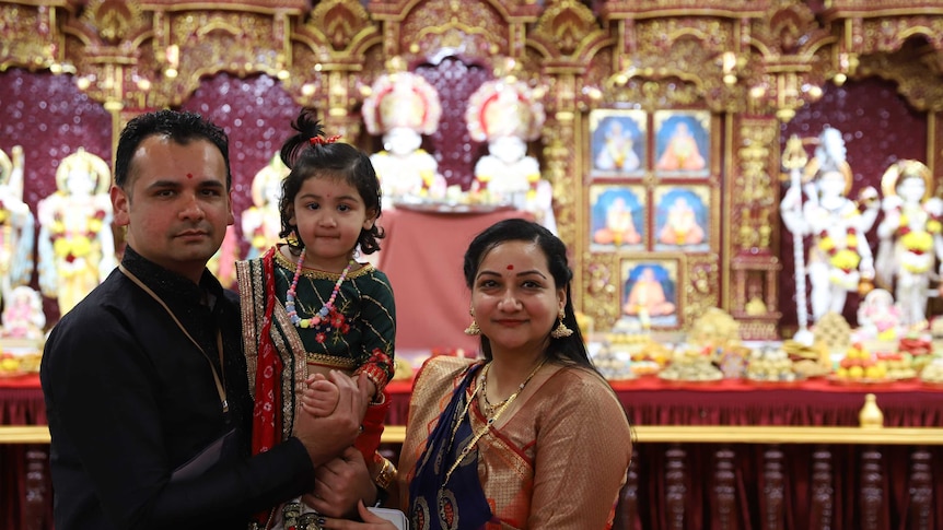 Young couple with their toddler, dressed up and serene in front of elaborate golden altar.