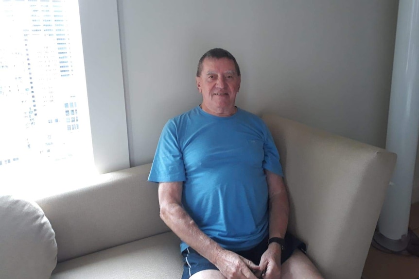 Alan Giles sits on a sofa wearing a blue t-shirt.