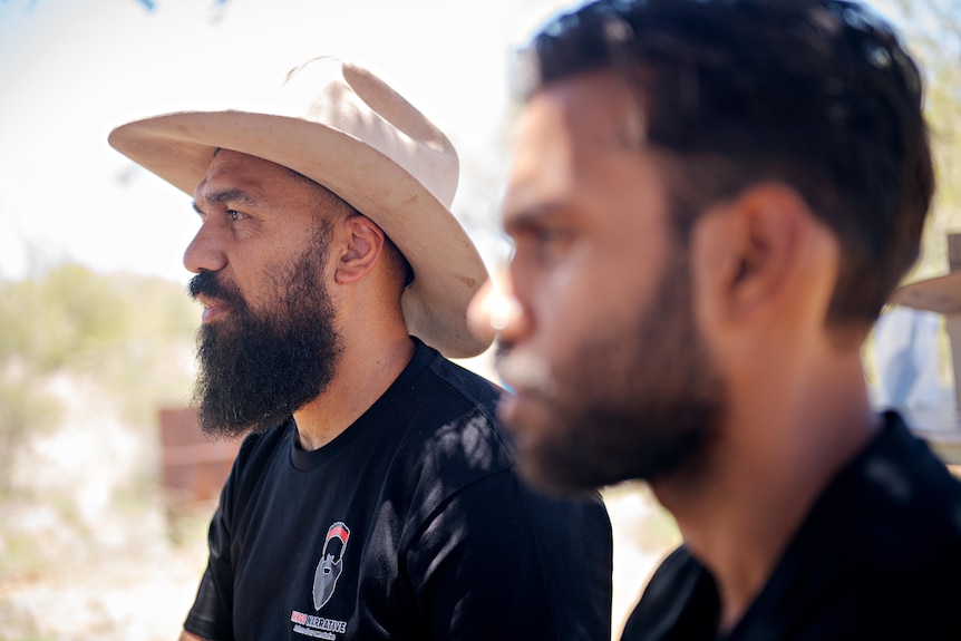 A man with a beard and wide-brimmed hat from the side. 