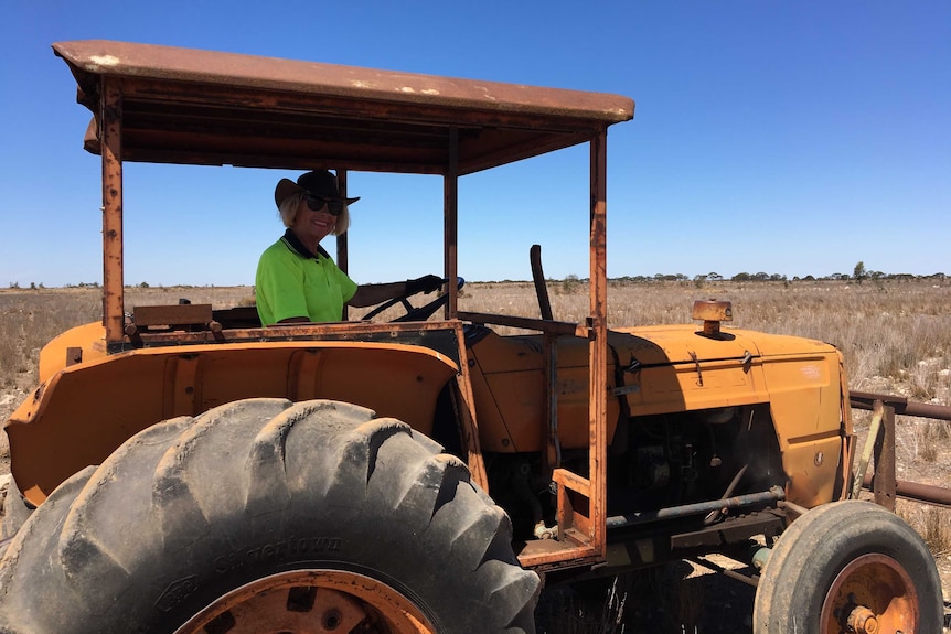 Woman with blonde hair, wearing high vis workwear sits in the cab of a tractor.