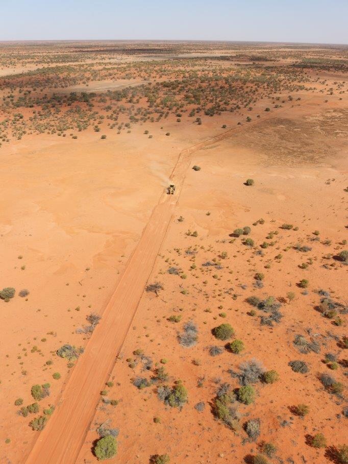 An aerial view of land cleared for a fence through red dert.