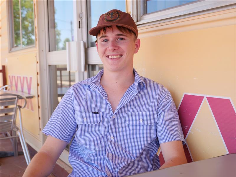 Um jovem está sentado em uma cadeira com um boné marrom.