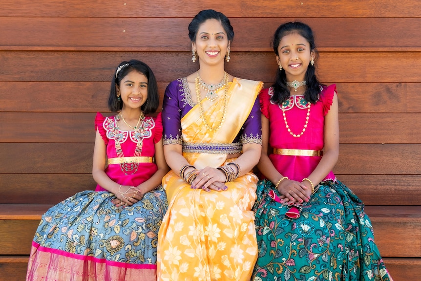 A woman with a daughter on her right and left, seated altogether smiling at the camera