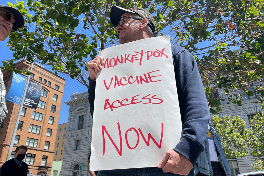 A man holds a handwritten sign that says, monkeypox vaccine access now. 