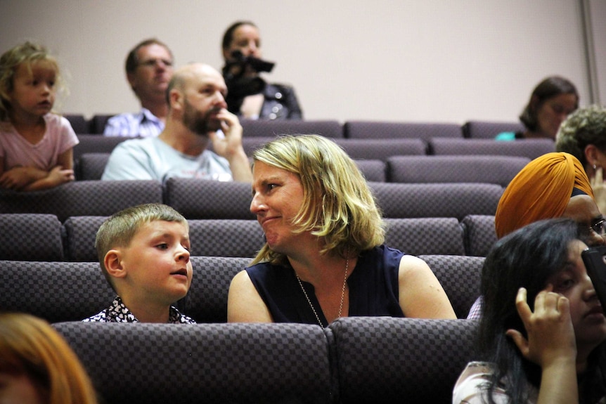 A woman making a sad face to another onlooker, after her daughter made a spelling error.