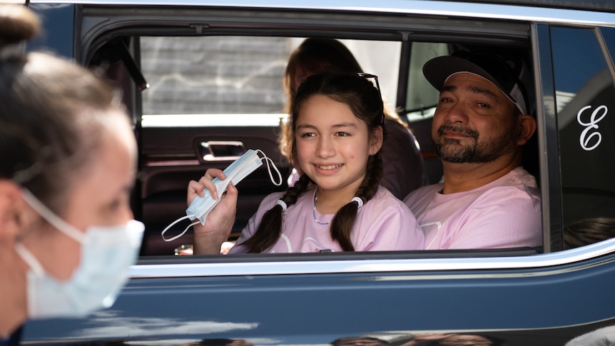 Young girl waves from a car as she leaves hospital