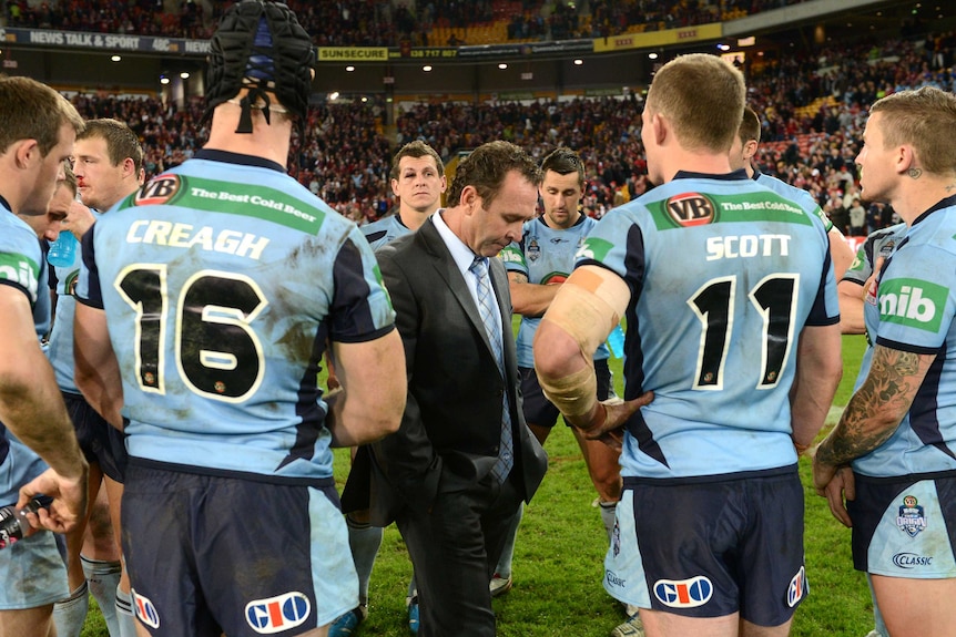 A dejected rugby league coach is surrounded by his players after losing a big game.