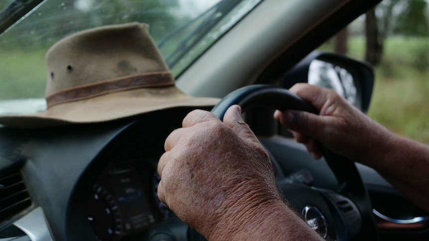 A man's weathered hands hold on to a steering wheel