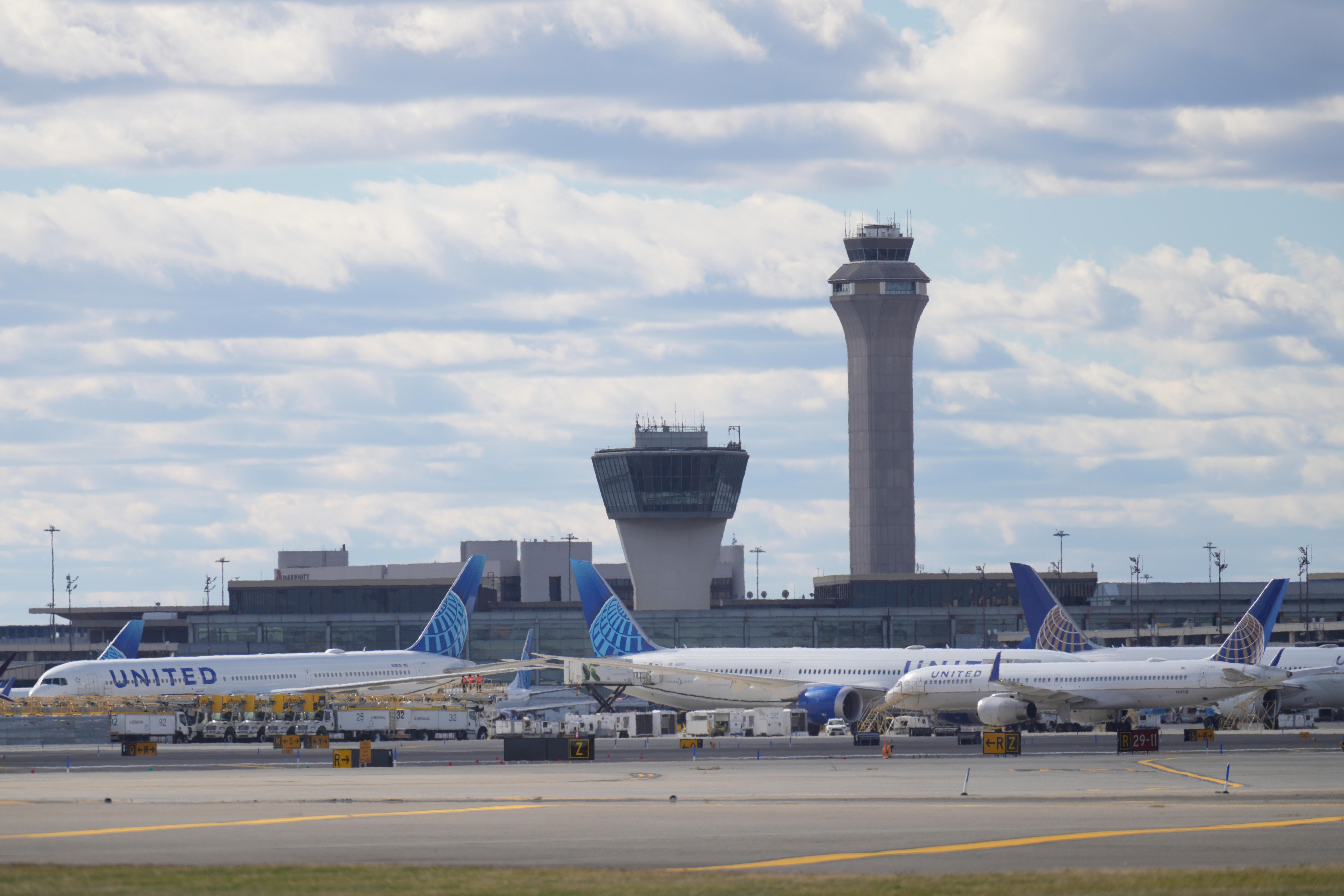 Blue and white United Airlines planes sitting motionless on an airport tarmac in front of air traffic control towers