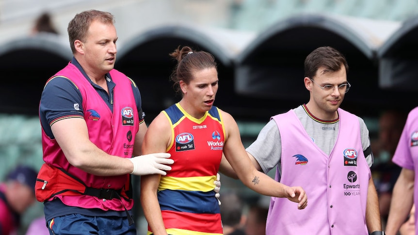 Chelsea Randall is attended to and escorted off the field by medical staff. 