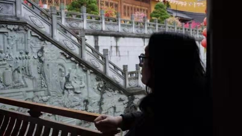 A woman in silhouette looks out over a Chinese temple.