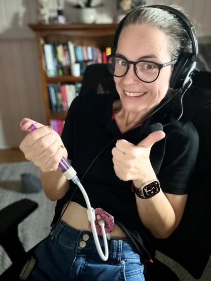 a woman feeding herself through a gastrostomy feeding tube, giving a thumbs-up