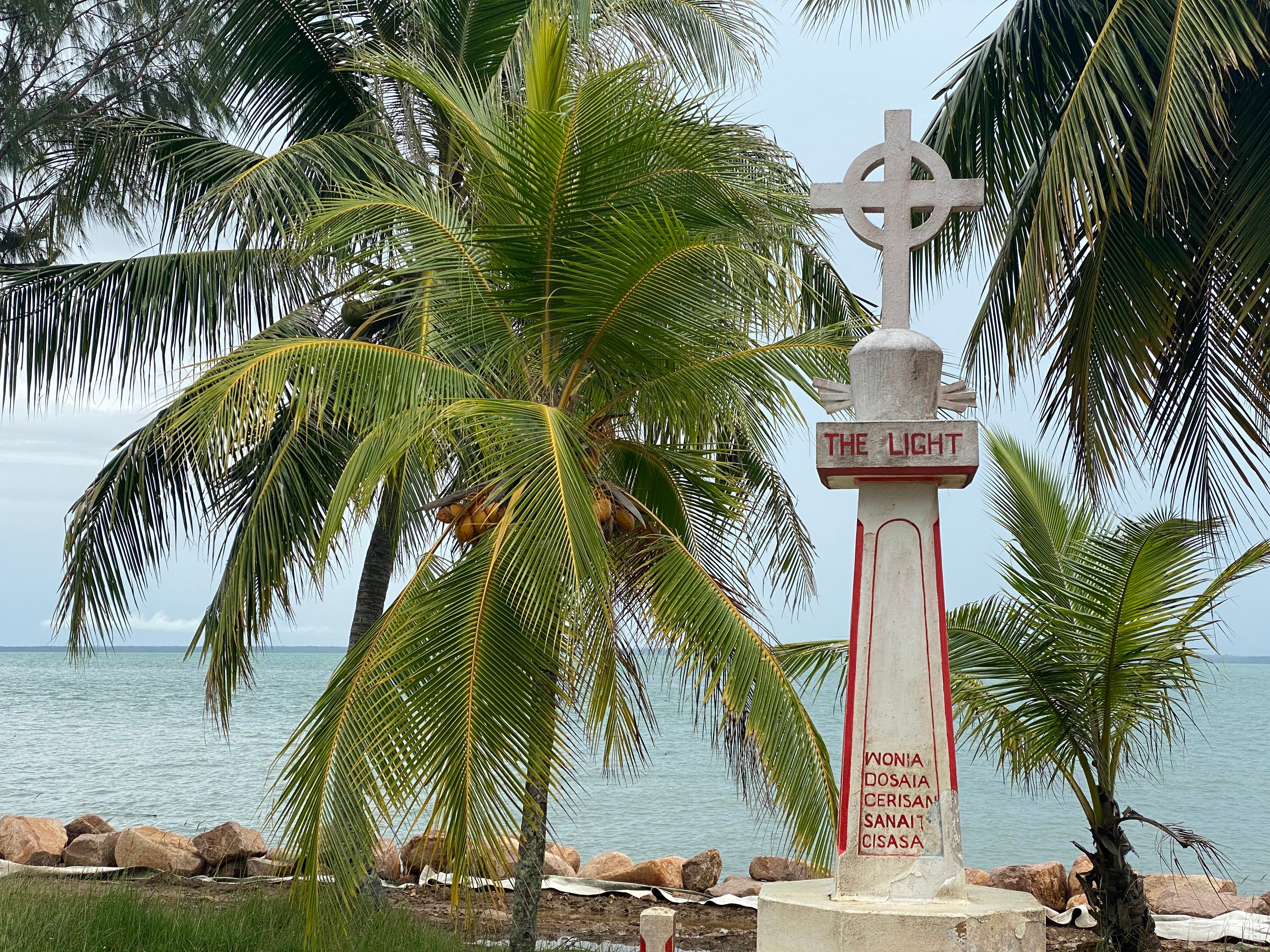 A monument on an island with the ocean and palm trees in the background. 