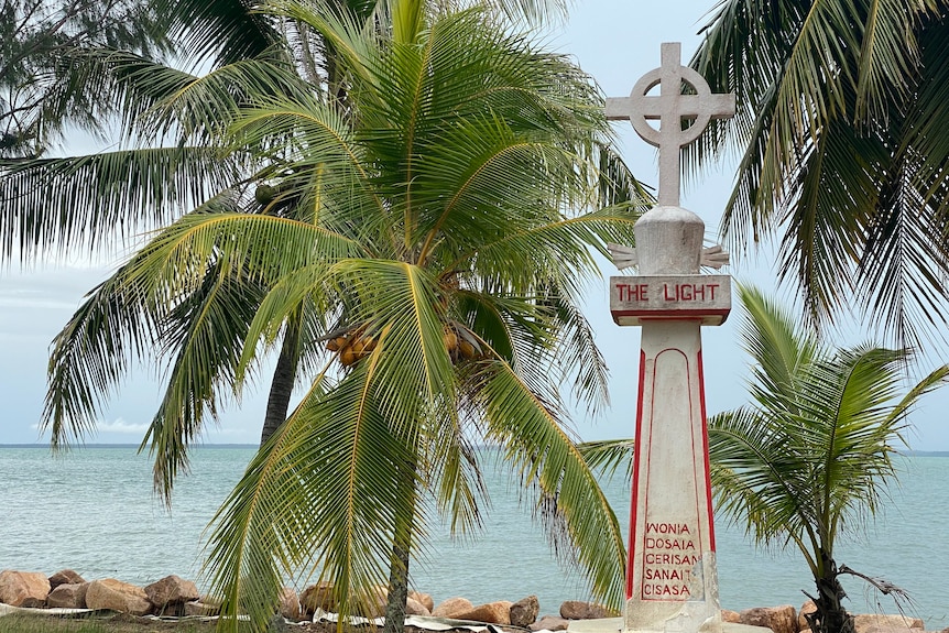 A monument on an island with the ocean and palm trees in the background. 