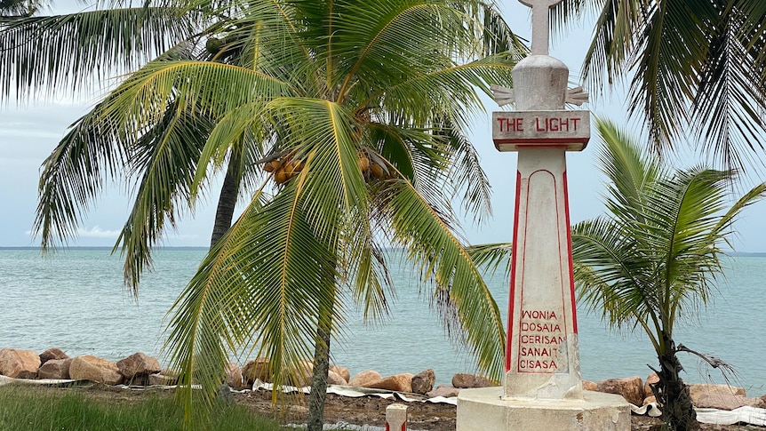 A monument on an island with the ocean and palm trees in the background. 