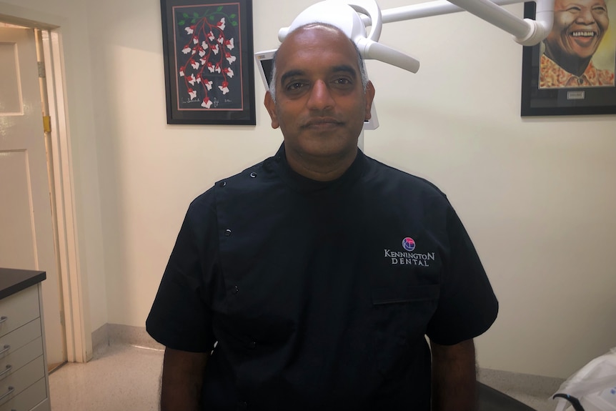 A dentist stands in front of a dentists chair.