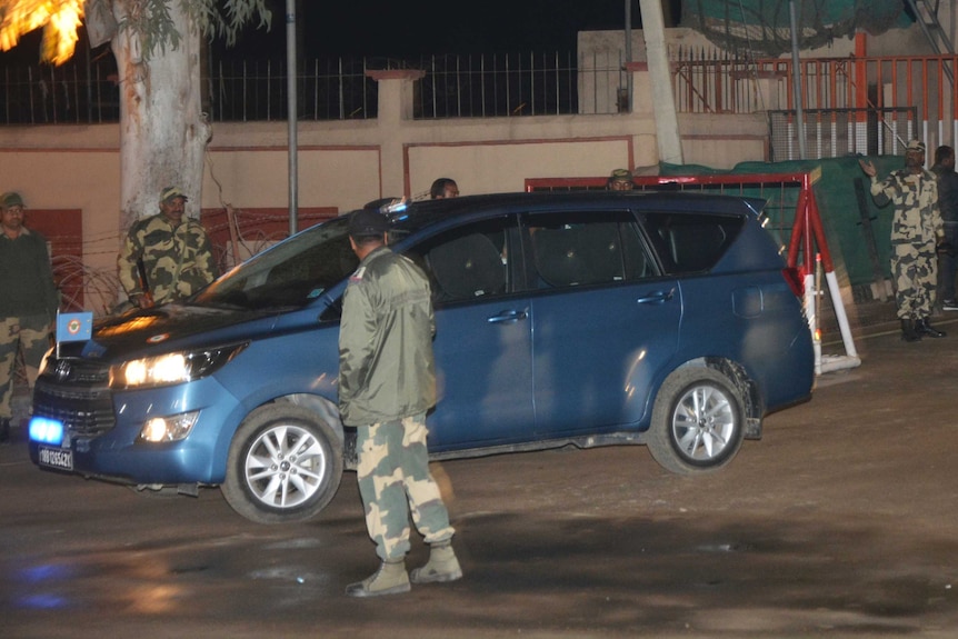 A blue van passes through a military inspection point, with soldiers standing outside
