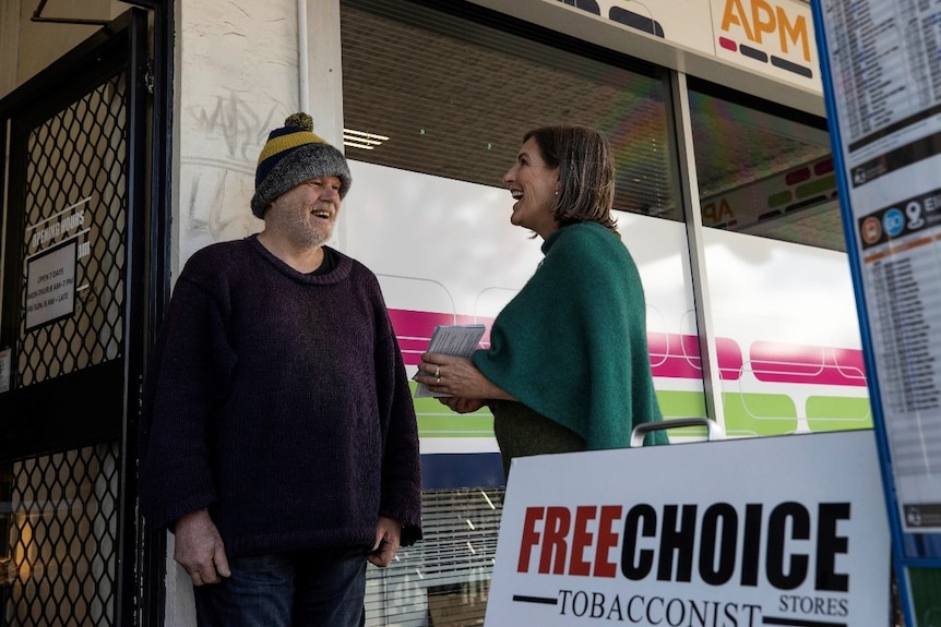 A woman speaking to a man outside a shop.