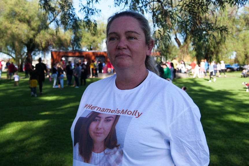 A woman standing outside in a park wearing a t-shirt with a photo of a young woman and the words "her name is Molly".