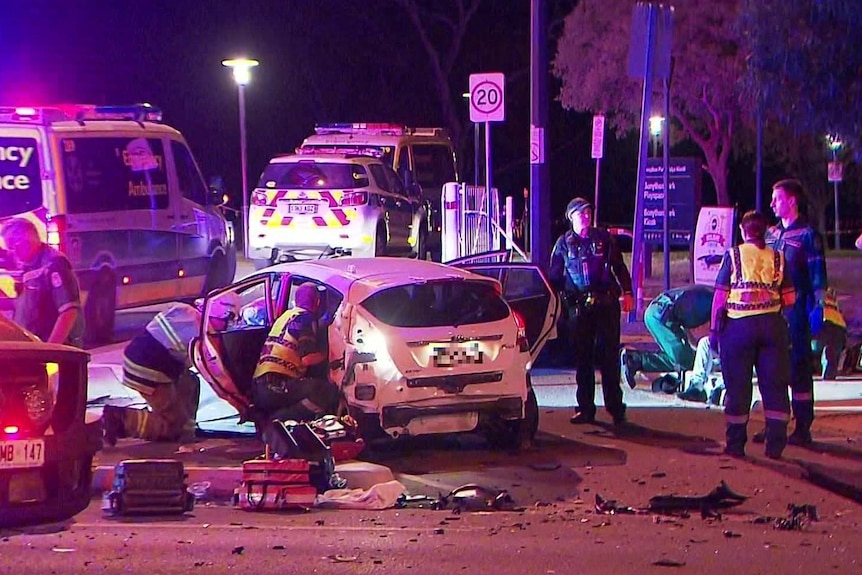 A small white car surrounded by emergency vehicles and personnel