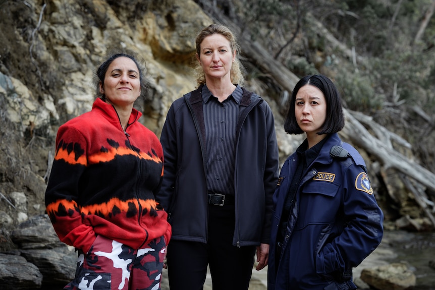 Three women, two in police uniforms, stand in a rocky landscape, in the TV series Deadloch