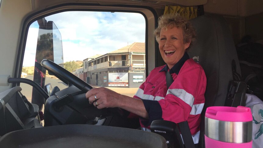 A laughing Heather Ewart holding steering wheel inside cabin of a truck.