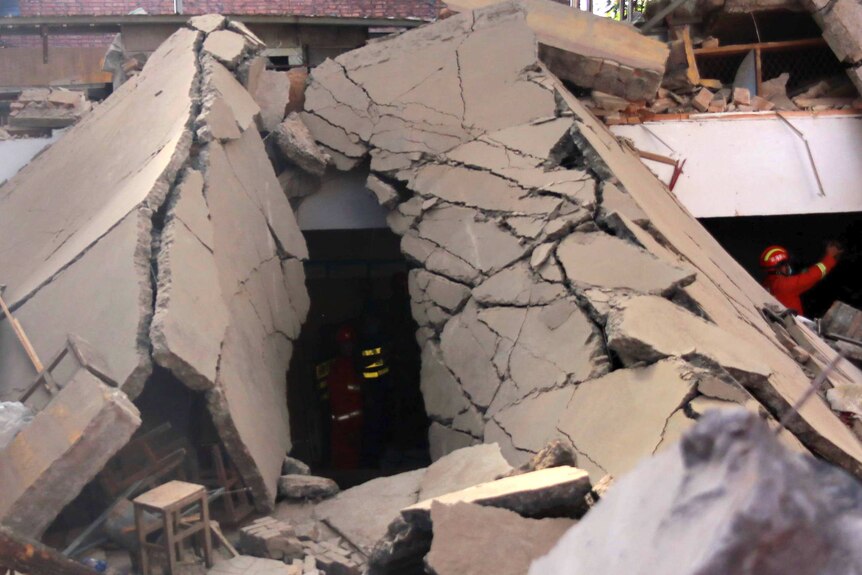 Rescue workers toil in the darkness under two large slabs of cracked, collapsed concrete.