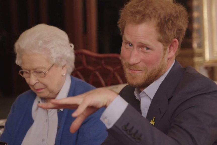 Queen looks at phone while Prince Harry pretends to drop microphone