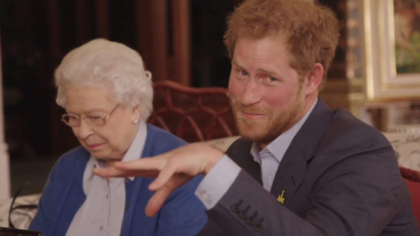 Queen looks at phone while Prince Harry pretends to drop microphone