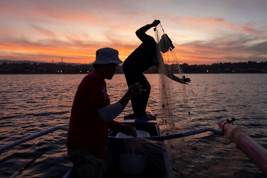 A person pulls a net from the water as another looks on. 