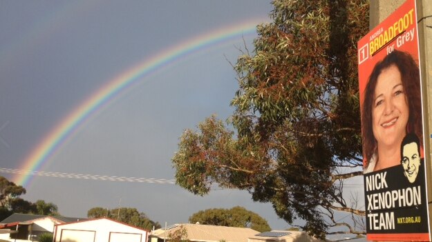 Nick Xenophon Team campaign sign hangs on a post with a rainbow in the background