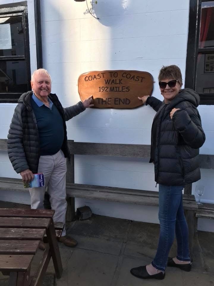 A man and a woman pointing to a wooden sign