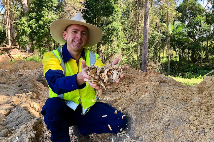 A man crouches, holding wood chips in his hands.