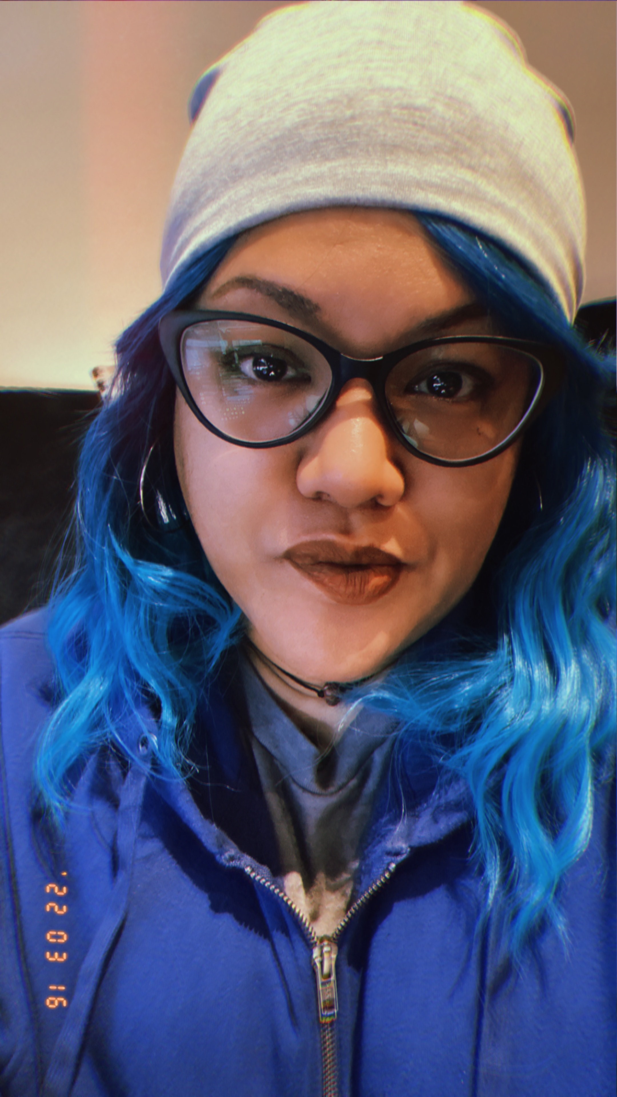 A woman with blue hair wearing a grey beanie and blue jacket 