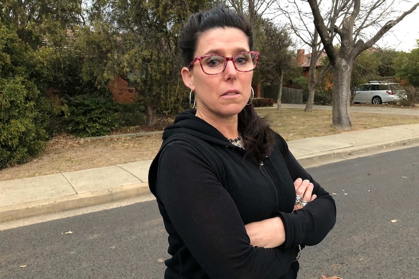 A woman stands with her arms crossed on the street.