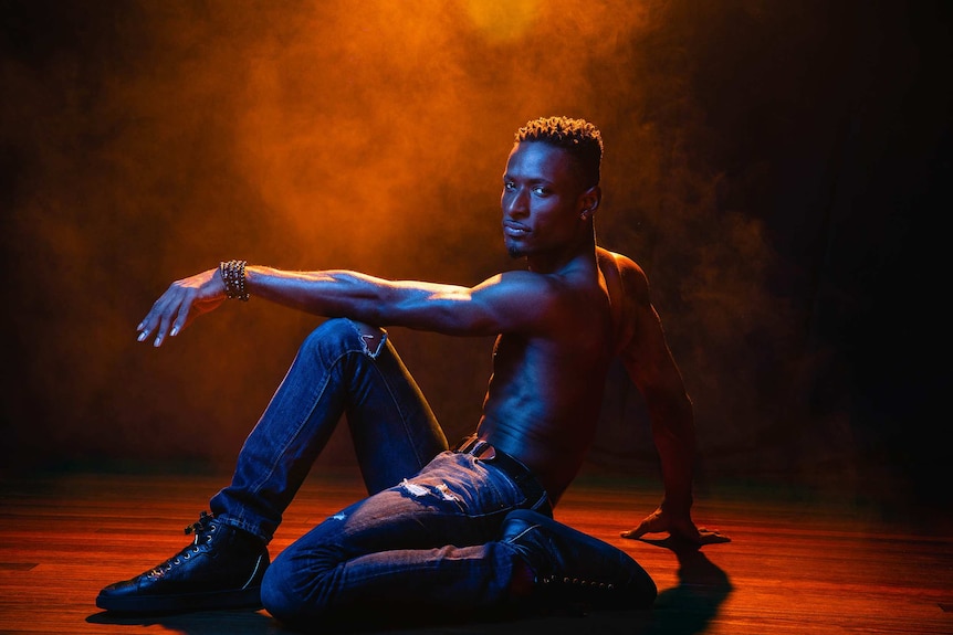 A dramatic colour wide photo of Dashaun Wesley in a dance pose on the floor in front of dark background.