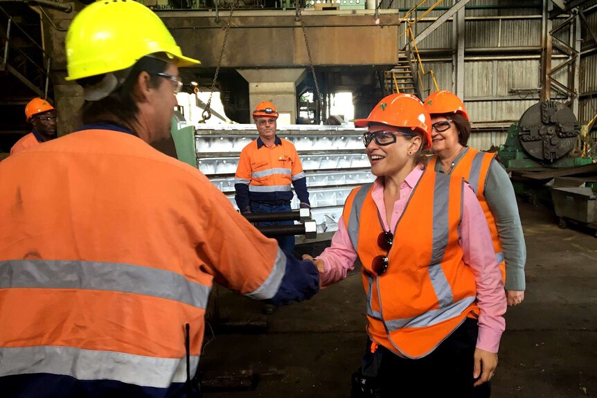 A woman in an orange hard hat shakes hands with a man who works in the sugar industry
