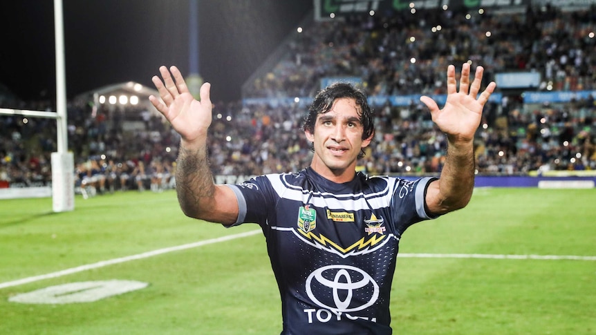 Johnathan Thurston waves both hands with a full stadium behind him