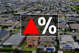 A red up arrow next to a percentage sign on top of an aerial view of dozens of houses.