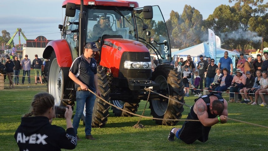 A man with big muscles has a chain around him and is pulling a bright red tractor.