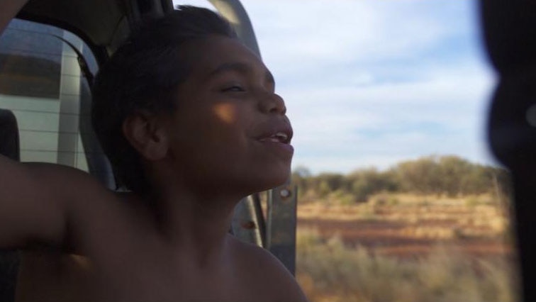 Indigenous boy smiles while riding on the back of a ute