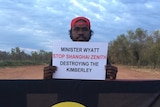 Man in red cap holding up sign, standing in middle of red dirt road