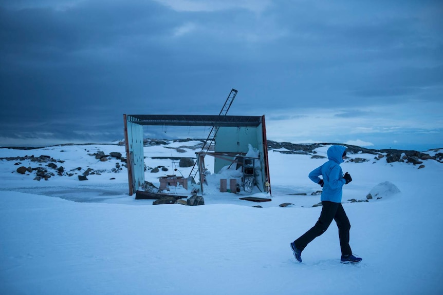 A woman rugged up in cold weather gear runs through snow